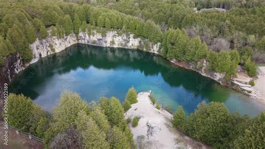 A wide aerial shot of the historic Elora Quarry Conservation Area in Ontario, showcasing its two-acre emerald swimming hole encircled by dramatic 12-meter limestone cliffs and dense forest