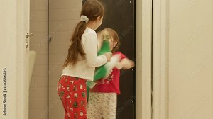 Small children in Christmas pajamas are holding green large socks for gifts in their hands, waving them at each other, fighting, laughing, having fun.