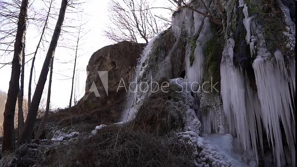 A frozen waterfall on a mountain river. The Bigar waterfall below Stara Planina is bound by ice, you can see ice stalactites and other ice forms, and some unfrozen water falling. The camera is static
