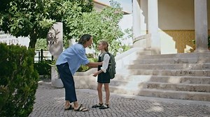 Mutter wartet Schulmädchen nach dem Unterricht. Kleines Kind mit Rucksack laufen Treppe umarmt liebevolle Mutter an sonnigen Straße. Glücklich überglücklich weibliche Eltern treffen kleine Kind Umarmung. Familienkonzept