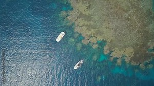 Aerial smooth movement of a coral reef in the Red Sea, with tourists in two boats near Jeddah in Saudi Arabia. Blue, green and turquoise waters