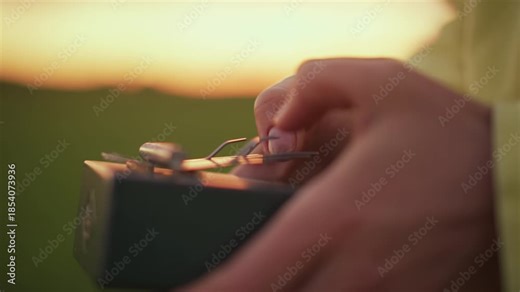 hands adjust light meter at sunset in meadow, photographer calibrates analog exposure meter with careful fingers, warm golden glow, shallow depth of field, tactile closeup of vintage device