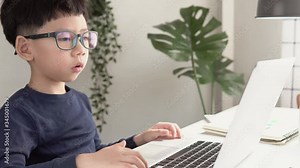 Social distancing & Online learning concept, Cute little Asian student kid type on computer and confused about online gamification lessons at home during Covid-19 pandemic lockdown and school closure.