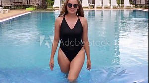 A plus-size woman with a sporty figure comes out of the pool in a black swimsuit