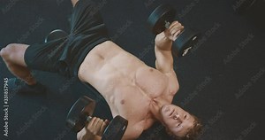 Strong muscular man lifting weights in the gym, weightlifter doing dumbbell presses and achieving his fitness goals