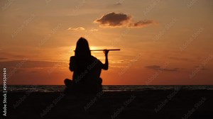 Silhouette of a beautiful man with long hair playing on flute in front of sunset. Slow motion. Enlightenment