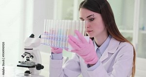 Woman scientist assesses test tubes filled with colored liquids. Researcher examines each to understand different reactions and properties exhibiting