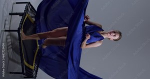 beautiful dancer in long evening blue dress jumping on trampoline, creative art, ballet on air, dancing and sport Slow motion Vertical view lifestyle free spare time, ballet girl has fun in studio