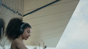 Young sporty woman in activewear and headphones setting up fitness tracker app on smartwatch and running away while training outdoors in city