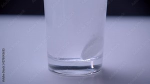 Closeup shoot of pill dissolving on the bottom of transparent glass standing on the white table