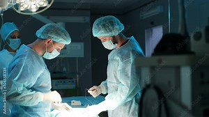 Multiethnic team of professional surgeons and nurse in uniform at work in operating room, performing heart transplant surgery operation under bright lamps. Teamwork surgeon in operating room, slowmo.
