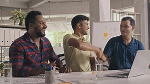 Medium shot of Indian software developers looking at laptop screen, then getting excited, clapping hands, high fiving and giving handshakes while celebrating successful IT project in office