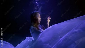 a beautiful brunette with long hair slowly descends into a cloud of white cloth in the darkness under the water. blue contour light