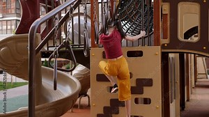 A little girl is playing on the playground, she climbs the stairs to the slide.