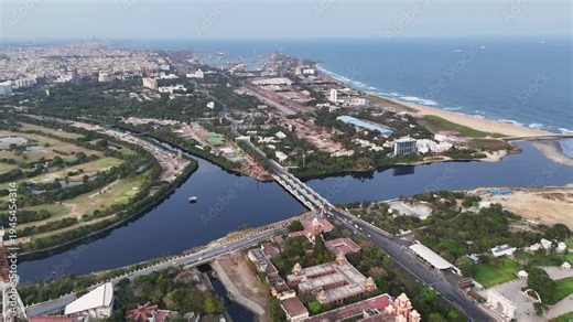Drone shot above Island Grounds in Chennai, highlighting the looping river, open green fields used for exhibitions, the old Doordarshan TV tower, and nearby heritage buildings and city roads.