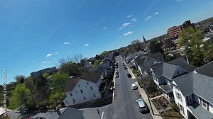 Drone fpv flight over houses at street of american town in spring. Sunny day with blue sky in Ephrata, PA, USA. Approaching flight.
