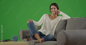 Portrait of lovely millennial girl posed sitting on couch with greenscreen background. woman sits on her couch with Chroma key.