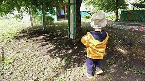 A child with a model car near the kindergarten fence. A little boy wants to communicate and play with his peers. Concept of preschool education, child safety, socialization, development, loneliness