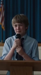 “They let the janitor’s kid talk now?” The whisper cut through the auditorium like a blade. A few laughs followed, quick and careless. On stage, the boy froze with the microphone still hovering near his mouth. The light above him was too bright. Too hot. Hundreds of eyes pressed into his back. Down in the seats, a man in a faded gray uniform stood up instinctively. His hands were rough, shaking, unsure where to rest. A teacher turned sharply. Someone sighed. Someone else looked away. The princip