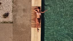 Video of a young woman sunbathing by the swimming pool. Aerial view.