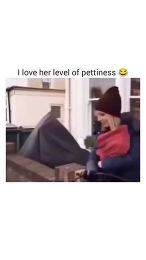 Explainers ZoneTM on Instagram: "The video captures a brief, quiet moment on a city street, beginning with a woman seated on a brick ledge, wearing a maroon beanie, a blue jacket, and a red scarf. She is engaged in a conversation with a man in a black coat with a fur-trimmed hood. The setting features a backdrop of buildings, a brick wall, and a black garbage bin, with the camera remaining static throughout. At 00:01, the woman remarks on the baby’s cuteness and asks about its age, to which the 