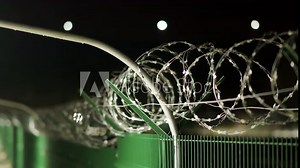 Perimeter security fencing system, razor wire fence with lighting at night, welded wire mesh fence line.