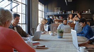 Interior of busy coffee shop with customers sitting at tables working on laptops - shot in slow motion