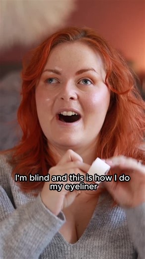 I’m blind, this is how I do my eyeliner ✨ Video description: Lucy with her makeup already done sits by her bed. She sticks makeup tape to her hand and removes it before doing that twice over to remove the stickiness. She then feels for her brow and eye to find where to stick the tape to her face for the best line. She then gets a fairly new (this is important) eyeliner pen and follows the contour of her lash line and the tape to draw a confident line. She repeats the process on the other side, t