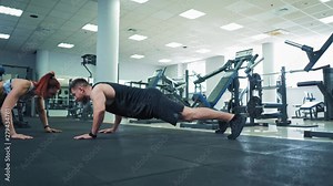 Fit couple doing push ups together in gym. Young sporty man and woman doing push ups and clap each other on the palm. Fitness studio.