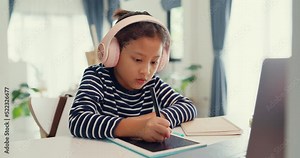 Asian toddler girl with sweater wear headphone sit front of desk with notepad use magic pen focus on writing do homework, finger counting number math online learning course from laptop at home.