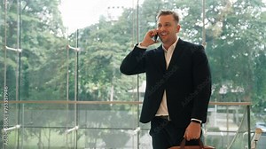 Skilled businessman calling manager while standing near modern glass door. Caucasian project manager talking to marketing team and planning financial idea or discussing about startup project. Urbane
