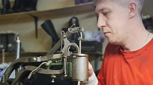 Caucasian male shoemaker adjusts the machine for sewing shoes with a strong thread. Ancient mechanical shoe repair machine