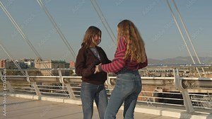 Happy female friends laughing and embracing while meeting on bridge on sunny day