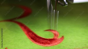 Sewing machine while embroidering with red thread on green background
