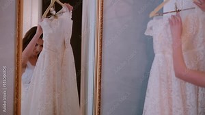Reflection in the mirror. Young woman takes off a wedding dress from a hanger. Morning preparing to ceremony.