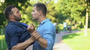 Angry men pushing and threatening each other outdoors solving problem with force