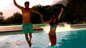 Happy couple jumping in swimming pool together in slow motion