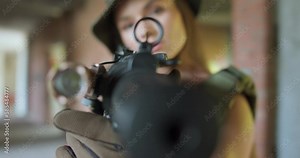 female sniper aims directly at the camera with a weapon, shooter is looking for a target, hunter is watching the prey, woman is preparing to shoot slow motion camera motion focus on trifle