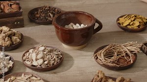 Traditional Medicine video sample with a close-up angle of Angelica sinensis being poured into a large bowl placed on a table with other herbal ingredients.natural remedies, health and wellness,
