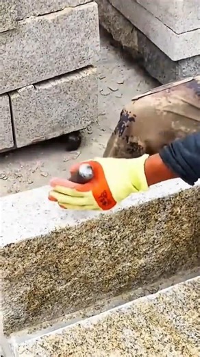 worker in gloves applies adhesive to a large stone block for construction
