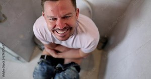 A smiling man sits on the toilet, slowmotion. Defecation problems, male health, shallow focus Stock ビデオ