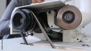 A close-up view of an industrial sewing machine being used in a workshop. The operator focuses on handling the fabric and machinery parts.