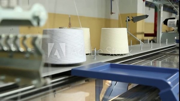 The knitting machine uses threads from bobbins mounted on top. A row of industrial textil flat knitting machines in a knitwear factory. Manufacture of knitwear, modern computerized flat Knitting Stock Video