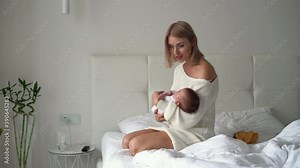 a young beautiful mother of European appearance is sitting in the room on the bed holding a newborn baby in her arms