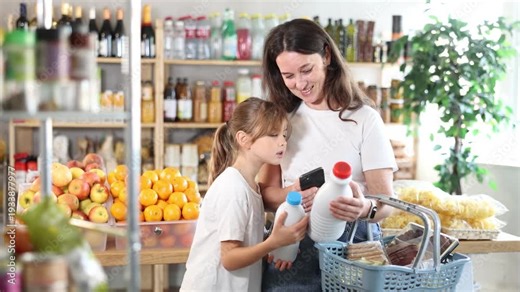 European girl with mother customers at shop scan QR code on milk package using phone camera. They study shelf life, learns calorie content of product using application. Visitor examines product