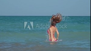 A woman in a pink bikini is performing a hair flip in the ocean, captured in slow motion video.