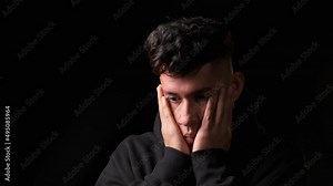 Worried man holding and covering his face with his hands while standing over a dark background.