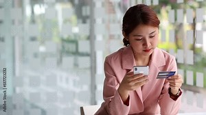 Asian woman holding credit card using mobile phone and entering payment code for online shopping.