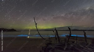 Time lapse of the Aurora Australis or Southern Lights over a lighthouse in Tasmania with neon blue bioluminescence in the waves breaking on the beach