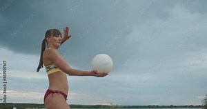 athletic woman dressed sporty bikini is playing beach volleyball, medium portrait at nature, striking ball